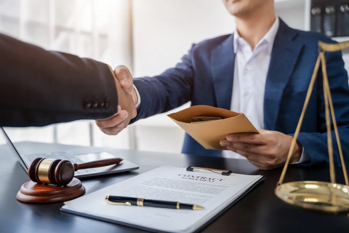 Anti corruption lawyers in Bangalore uncovering bribery—handshake with cash envelope beside gavel and contract.